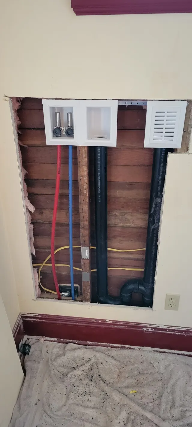 A new laundry supply box and drain, with red and blue PEX lines and black ABS drain, set into an opened wall of an older home.
