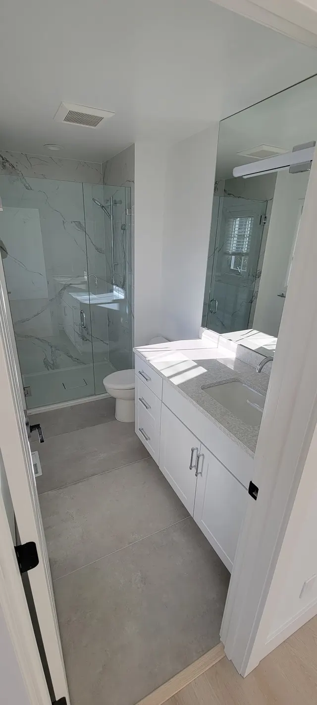 A finished white bathroom with a marble walk-in shower, white vanity with a stone top, and a new toilet.